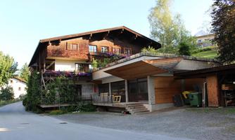 A beautiful house in alpine style with wooden cladding and colorful flowers. In the foreground, a modern covered terrace and a quiet street.