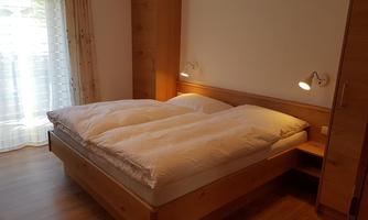A cozy bedroom with a double bed and wooden wardrobes. Natural light streams through the window, creating a welcoming atmosphere.