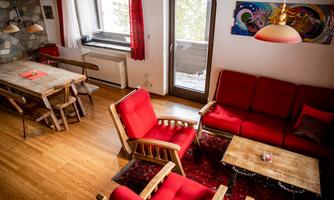 A cozy living room with red armchairs and a wooden table. Large windows let in plenty of light, creating a warm atmosphere.