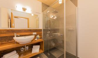 A modern bathroom with a glass shower and an elegant sink. Wooden shelves with fresh towels and care products complement the decor.
