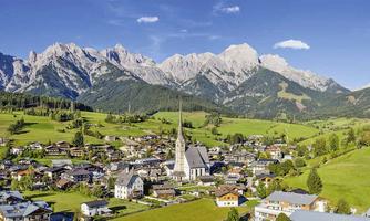 An idyllic landscape with a small village, surrounded by impressive mountains. The sky is clear and the meadows are green.