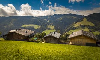 A picturesque mountain landscape with traditional wooden houses. The sky is blue and the meadows are green.