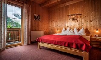 A cozy bedroom with wood walls and a large bed. The balcony offers a view outside, and the room is well-lit.
