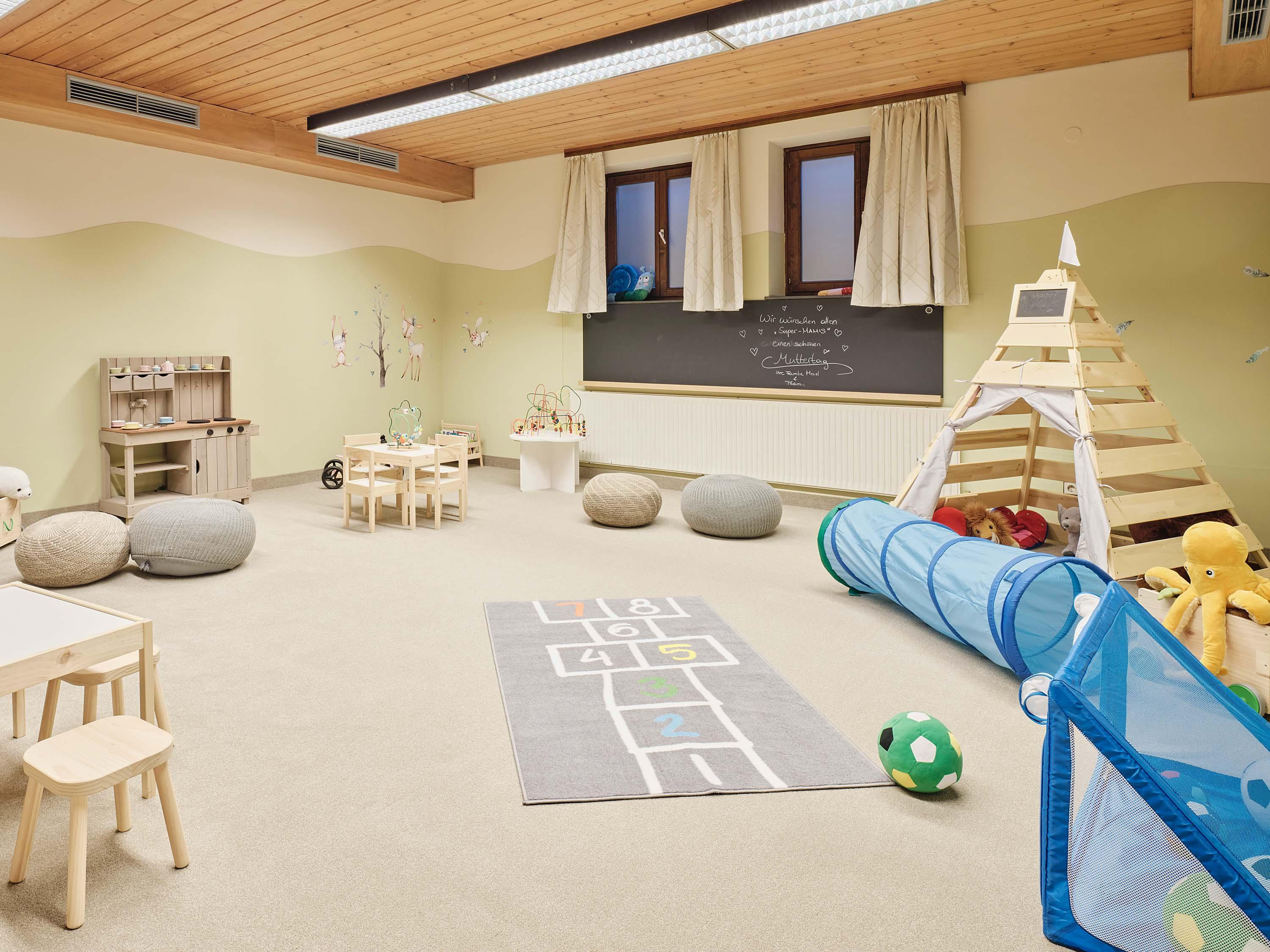 A bright and inviting playroom with various toys and a play mat. There are cozy seating areas and a play tunnel structure.