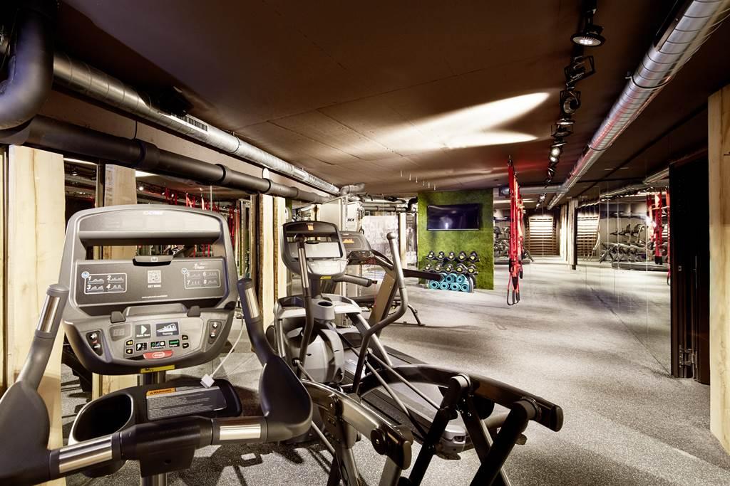 A modern gym with various workout equipment. The environment is well-lit and offers an open space for physical activities.