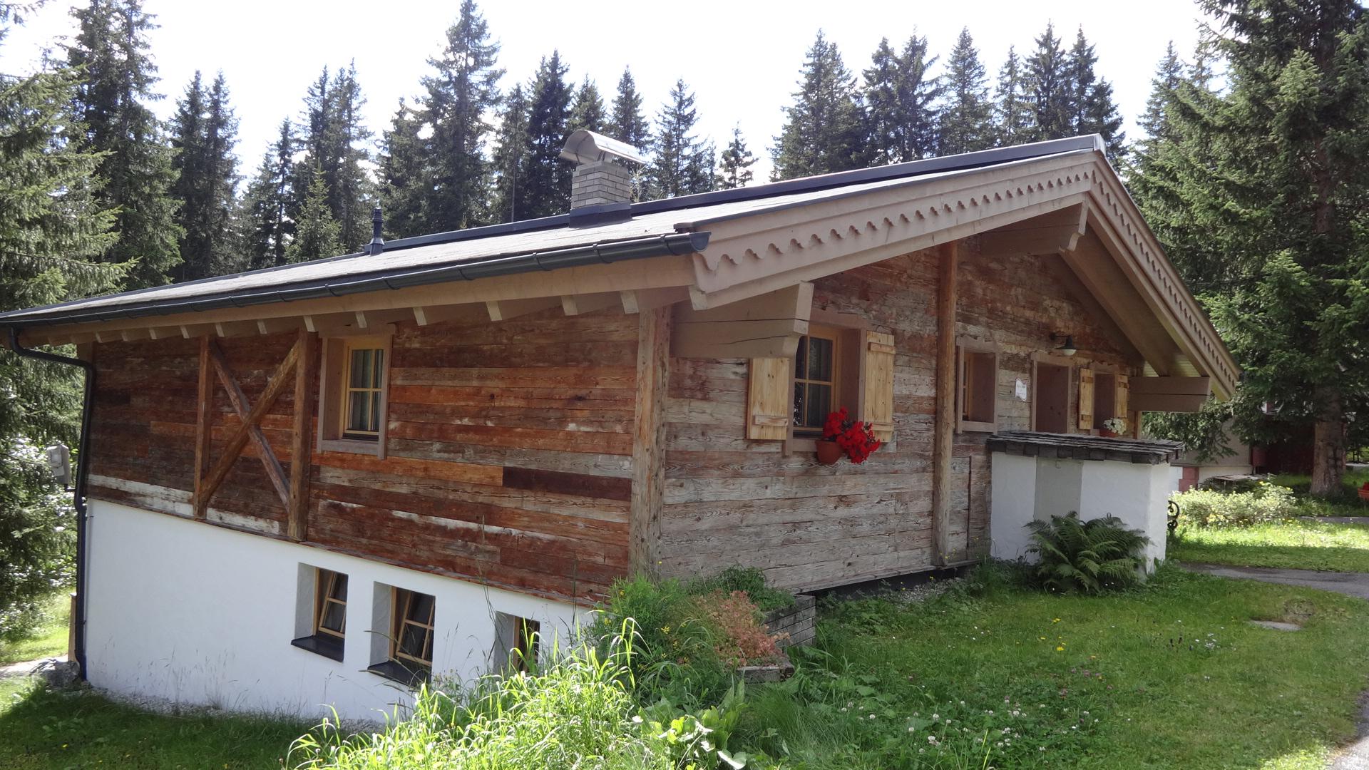 A rustic wooden house amidst trees. It has a green meadow and a rural charm.
