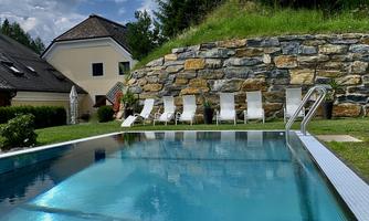A clear pool surrounded by a well-maintained lawn and sun loungers. In the background, trees and a building are visible.