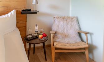 A cozy armchair with a soft cover is next to a small table. On the table, there are fruits and a glass of water.