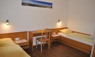 A simple room with two beds and a desk. The walls are light and there is a decorative landscape painting above the bed.
