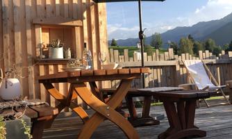 A cozy table with chairs under a sunshade. In the background, there are mountains and a clear sky.