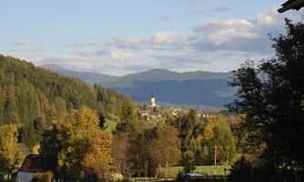 A picturesque landscape with gentle hills and colorful autumn trees. In the background, a small church can be seen in a quiet village.