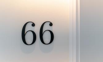 An elegant door number 66 in black font on a light wall. The depiction is simple and modern.
