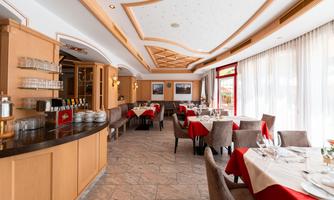 An elegant restaurant with wooden furniture and red tablecloths. Large windows let in plenty of natural light.