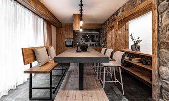 A modern dining area with a long wooden table and stylish chairs. The walls are made of natural stone and wood, creating a cozy atmosphere.