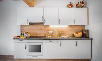 A modern kitchen with white cabinets and wooden details. On the countertop, there are fruits and drinks arranged decoratively.
