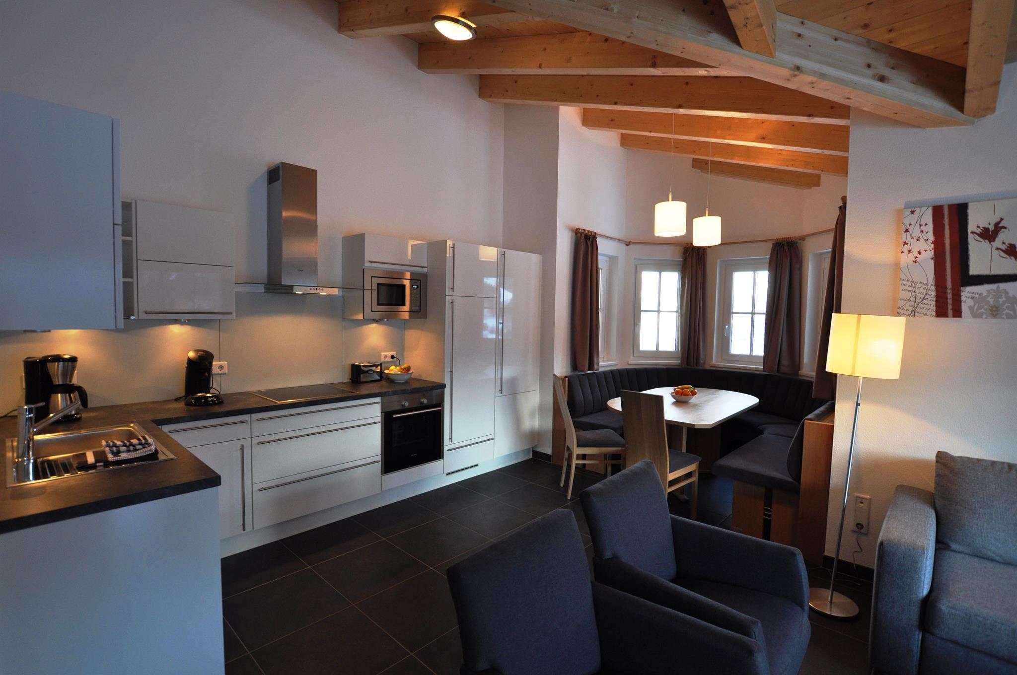 A modern kitchen with open shelves and stainless steel appliances. The living area is bright and inviting, with a dining table and cozy seating.