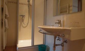 A small, modern bathroom with a shower and a sink. There are bright tiles and a decorative bath towel.