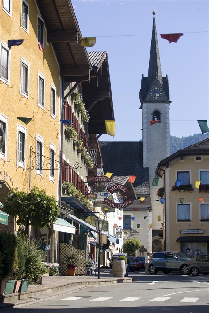 A picturesque street with colorful houses and a church in the background. Colorful flags hang above the street, creating a festive atmosphere.