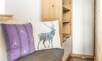 A cozy seating area with a gray sofa and decorative cushions. In the background, there is a wooden shelf.