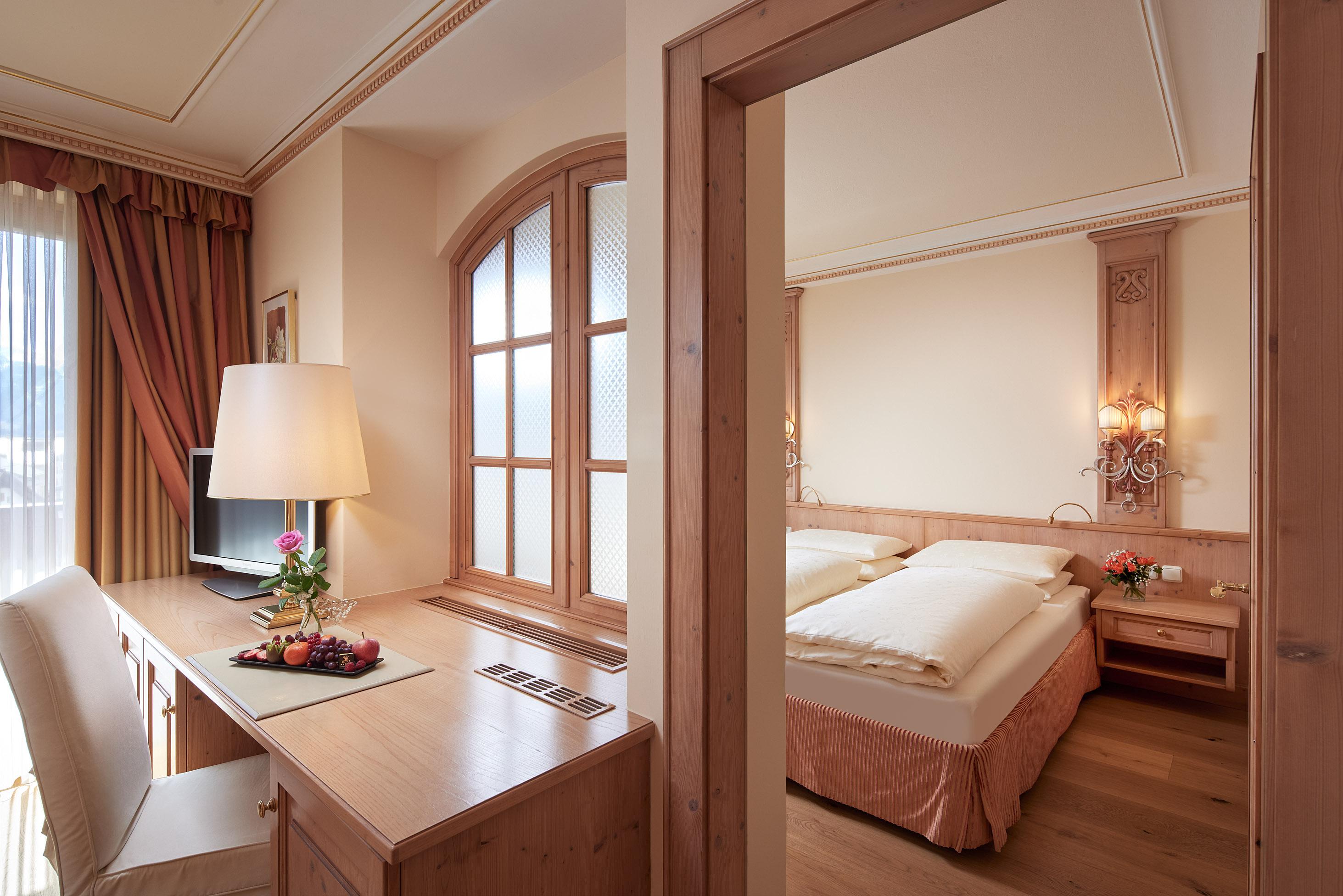 A bright hotel room with a double bed and a workspace. The decor is modern and cozy, with wood details and a window that lets in daylight.