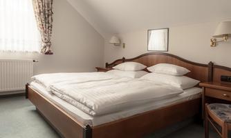 A cozy bedroom with a double bed and large pillows. The room has natural sources of light and a friendly, inviting atmosphere.