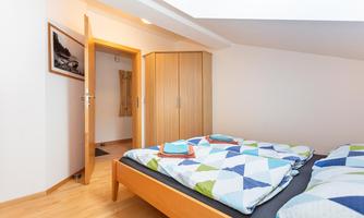 A cozy bedroom with a double bed and colorful blankets. The room has a bright atmosphere and an open wardrobe.
