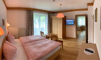 A cozy room with two single beds, pink pillows, and a television. Bright curtains and warm lighting create an inviting atmosphere.