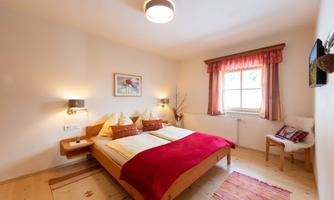 A cozy bedroom with two beds and red accents. Large windows provide plenty of daylight and an inviting atmosphere.
