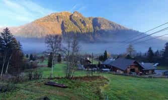 A picturesque landscape with a mountain in the background and misty fields. A few houses are gently nestled in the surroundings.