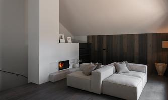 A modern living room with a comfortable sofa and an open fireplace. The walls are made of wood and the room has a bright, inviting atmosphere.