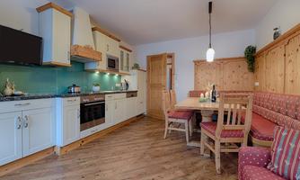A bright kitchen with modern appliances and wood paneling. There is a dining area with a large table and cozy benches.