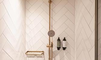 A modern shower with a golden showerhead and elegant tiles. The wooden ceiling accent adds warmth to the space.