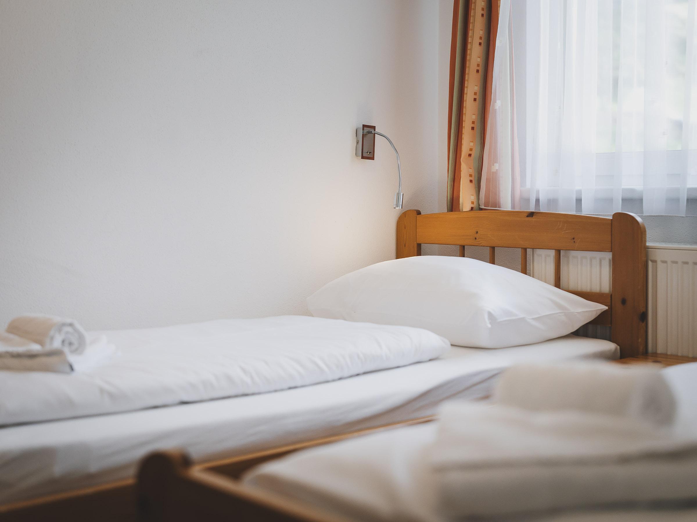 A simple room with two wooden beds and fresh bedding. The window lets in plenty of daylight.