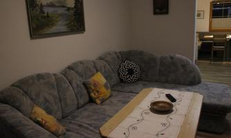 A cozy living room with a large, curved couch and a wooden table. A landscape painting hangs on the wall, depicting a serene nature scene.