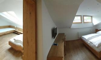 A spacious room with wooden interiors and two separate areas. There is a double bed, a desk, and a TV.