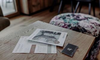 A table with several leaflets and a business card. The table has a wooden surface and seating furniture is visible in the background.
