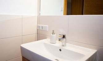 A modern bathroom with a white sink and a large mirror. The walls are adorned with light tiles.