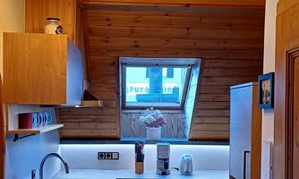 A modern kitchen with wooden shelves and a window front. The cabinets are in neutral colors and the floor is made of wood.