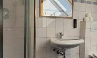A modern bathroom with a shower, a sink, and a large mirror. The walls are tiled and the floor has a blue covering.