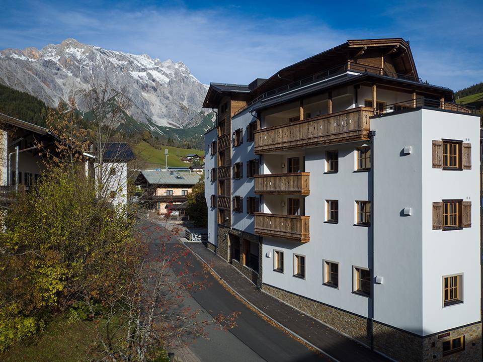A modern building in the mountains, surrounded by nature and a clear blue sky. Snow-capped mountains are visible in the background.