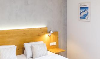 A modern bedroom with a wooden headboard and two pillows. A picture of snow-covered mountains hangs on the wall.