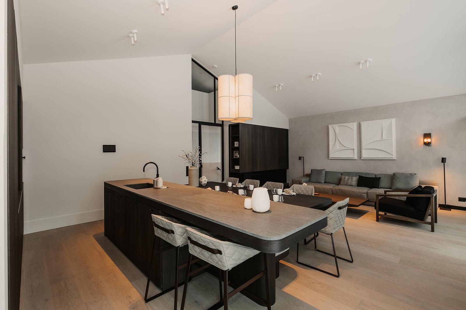 A modern kitchen with a large dining table and elegant stools. The open living area has a bright, friendly atmosphere.