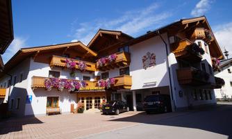 A charming hotel with traditional balconies and blooming flowers. The facade is painted in bright colors and offers inviting parking options.