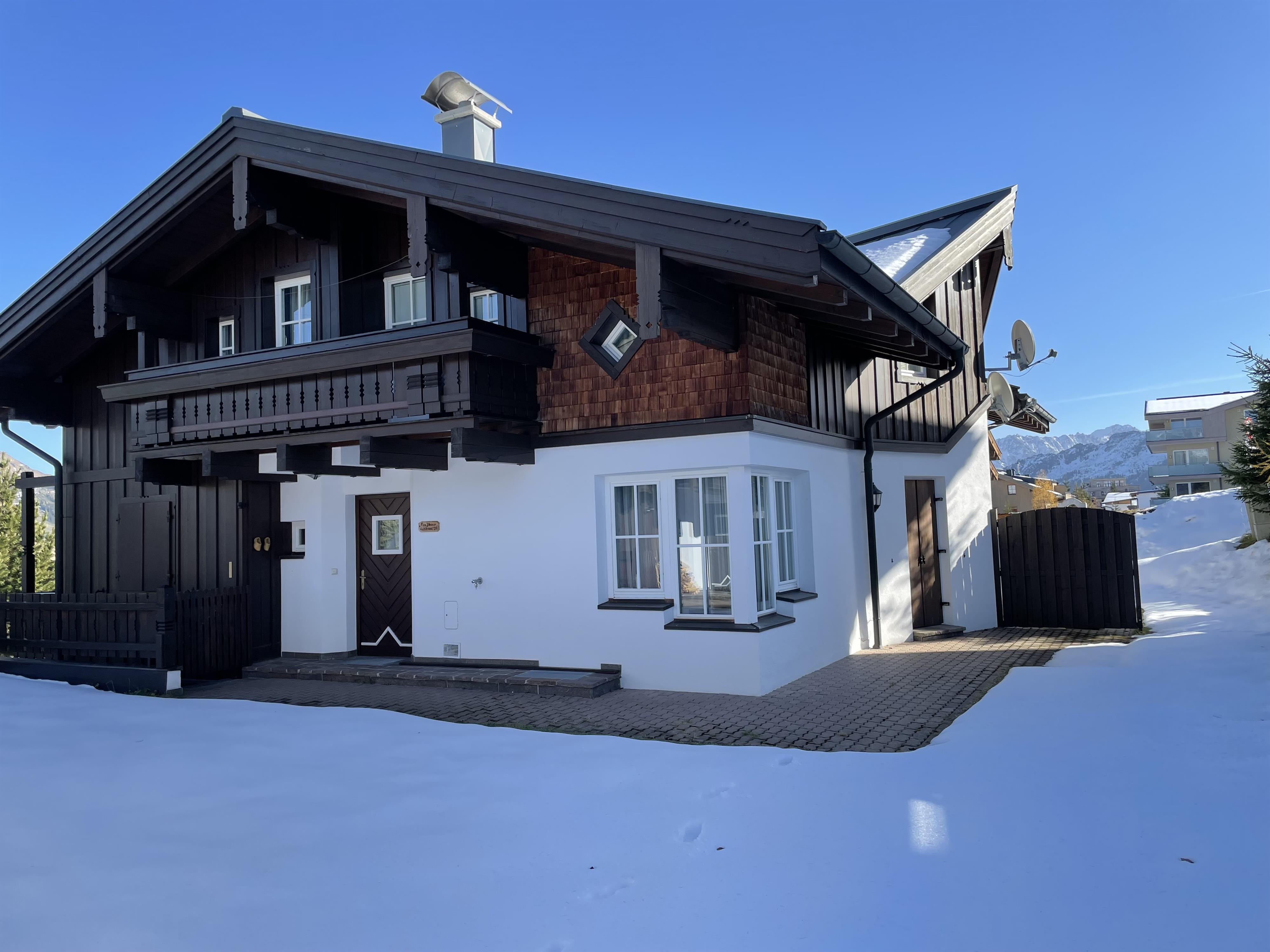 A traditional old house in the snow, surrounded by a serene winter landscape. The sky is clear and blue, providing a beautiful contrast to the white snow cover.