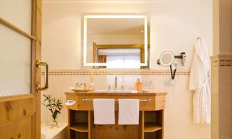 A modern bathroom with wooden furniture and a large mirror. Soft towels hang next to a sink, and the walls are bright and inviting.