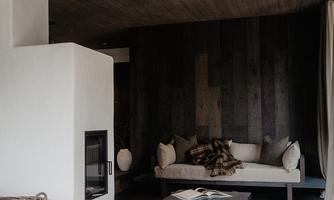 A modern living room with a bright, minimalist design. There is a cozy seating area and a fireplace, surrounded by warm wood and gray tones.