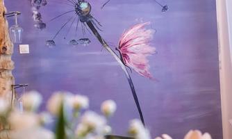 A colorful mural of a dandelion on a purple background. In the foreground, blurred flowers can be seen.