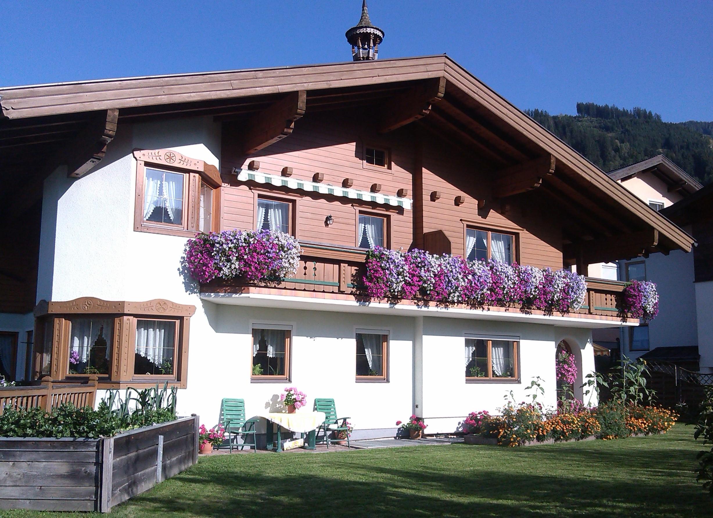 A traditional house with a balcony full of colorful flowers. The garden is well-kept and there are cozy seating areas outside.
