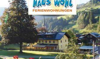 A picturesque landscape with a yellow building and green meadows. In the background, mountains and a blue sky can be seen.