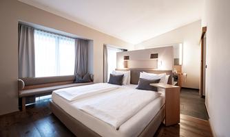 A modern room with two beds and soft colors. Light streams through the window and the atmosphere is inviting.